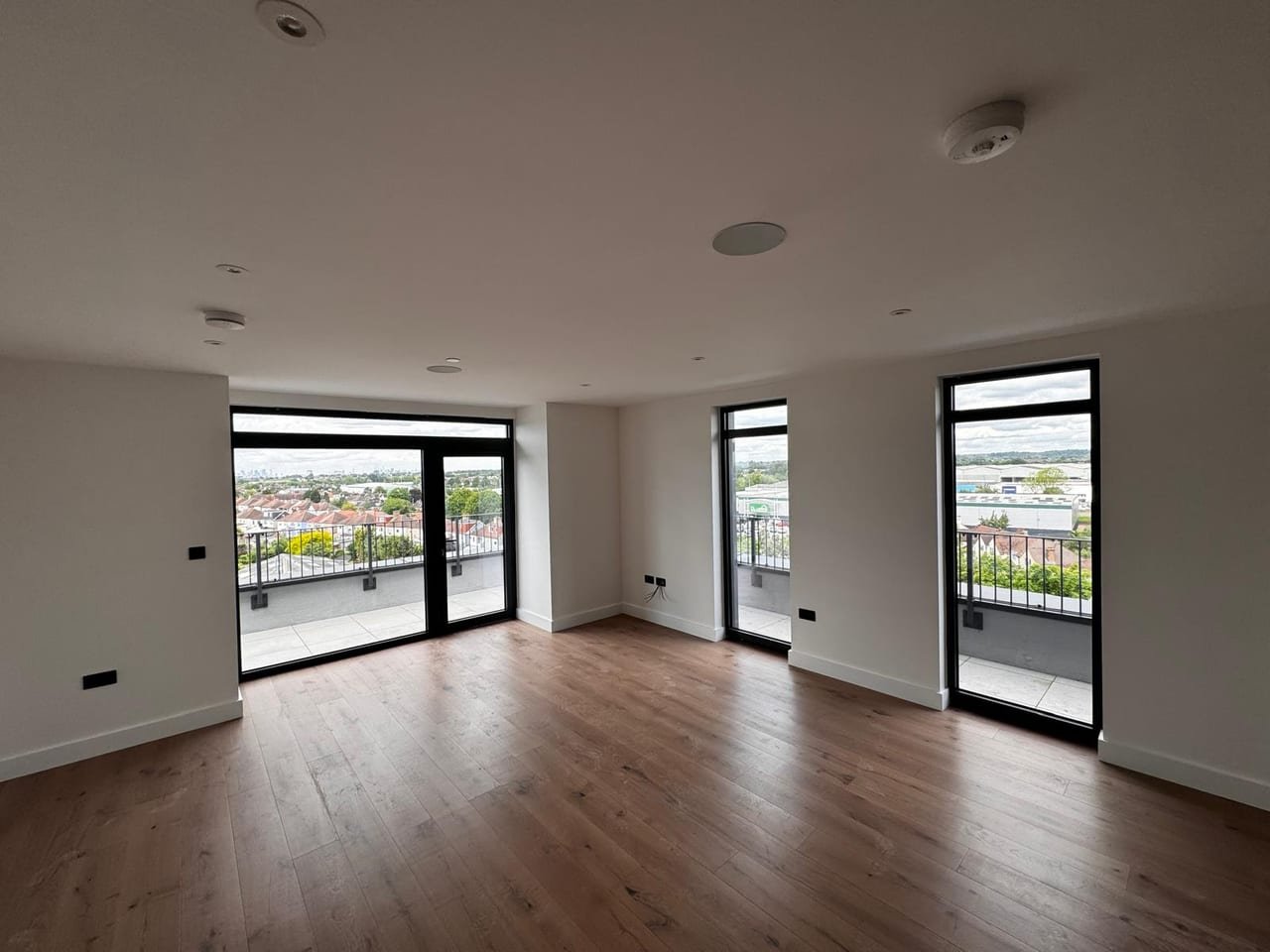 Empty apartment interior with oak flooring and three floor-to-ceiling glazed openings onto a balcony